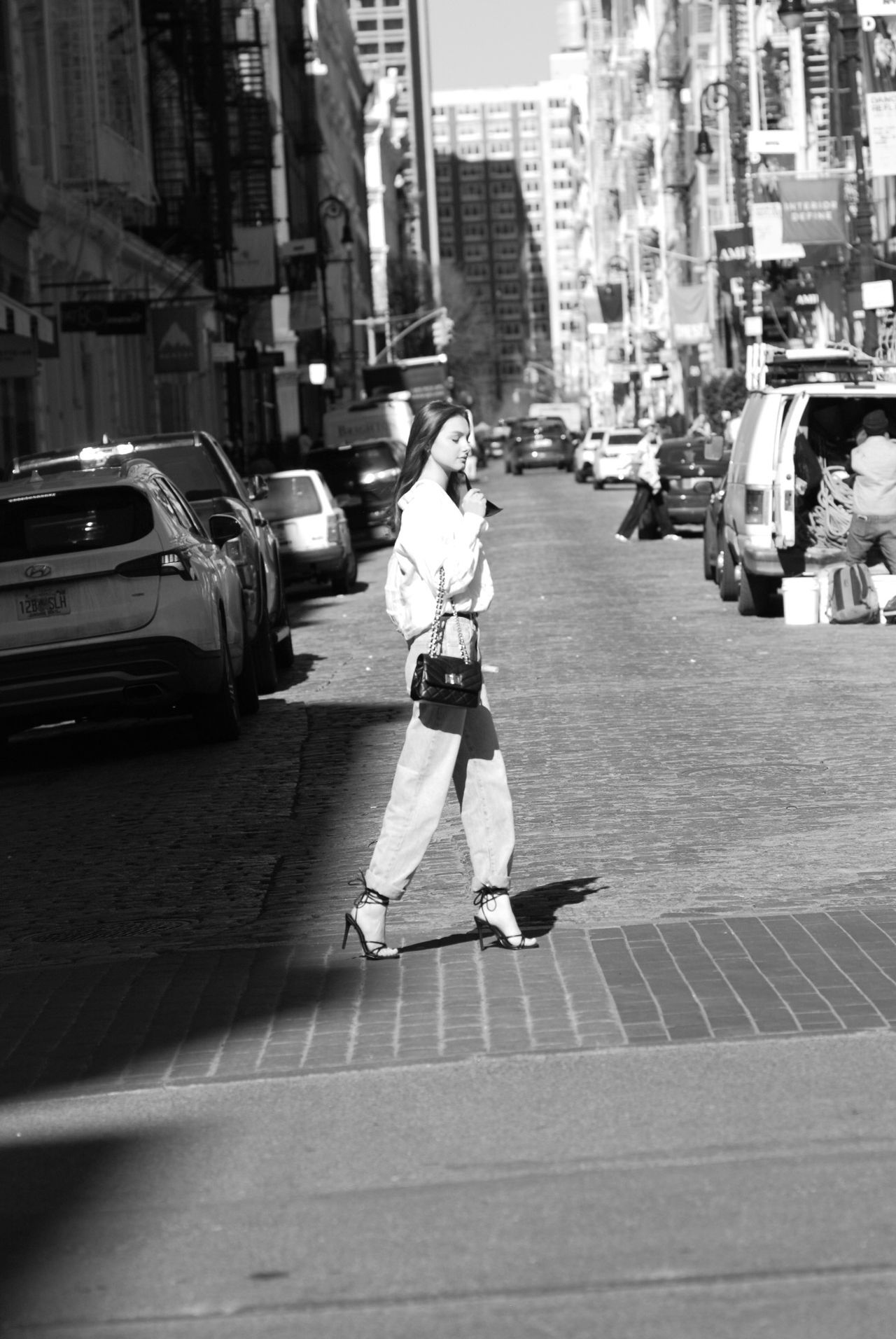 Mia Fantalin crossing a cobblestone SoHo street in black and white, in a white shirt and light wide-leg jeans
