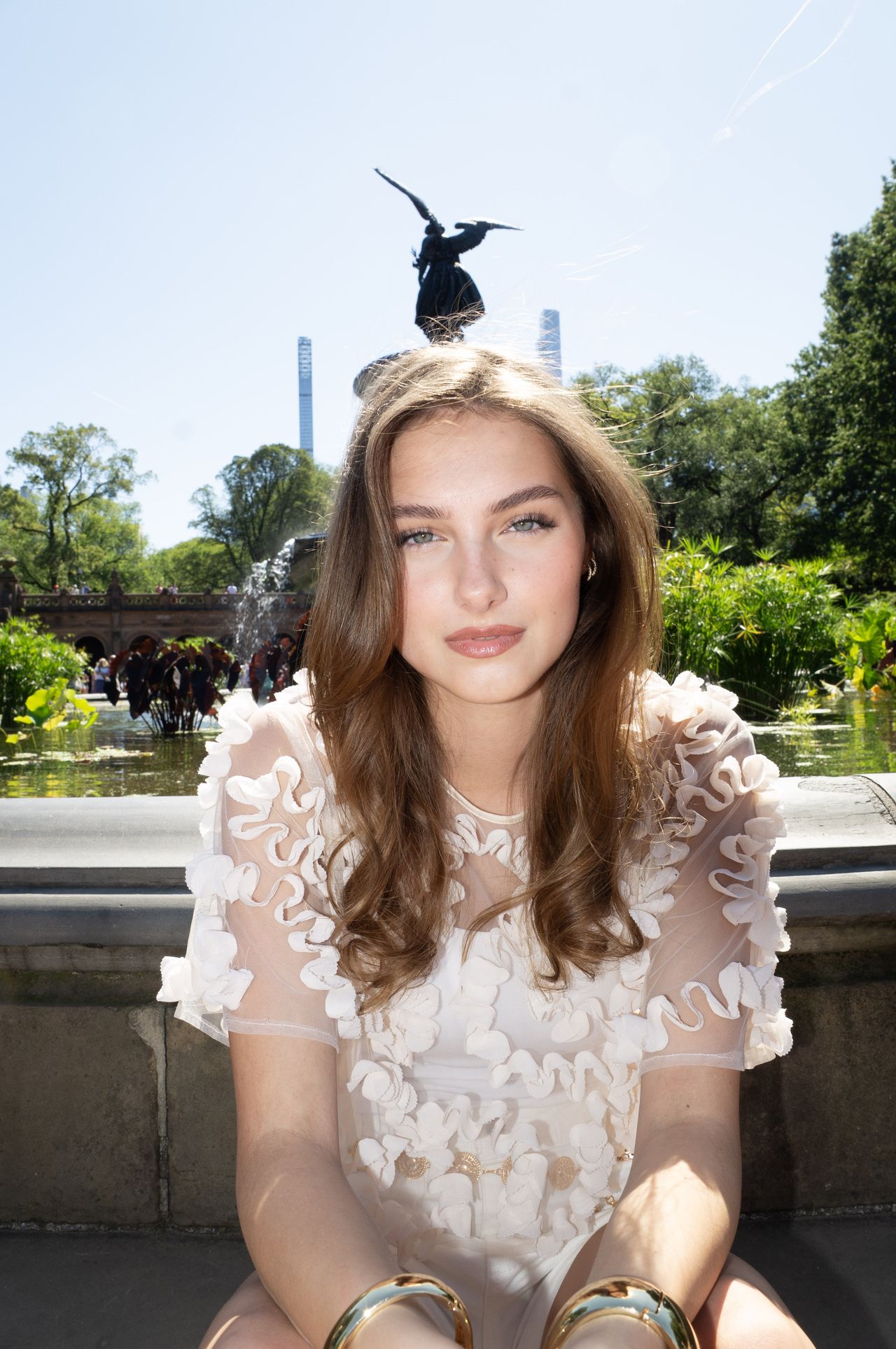 Mia Fantalin seated at Bethesda Fountain in Central Park, the Angel of the Waters statue rising behind her