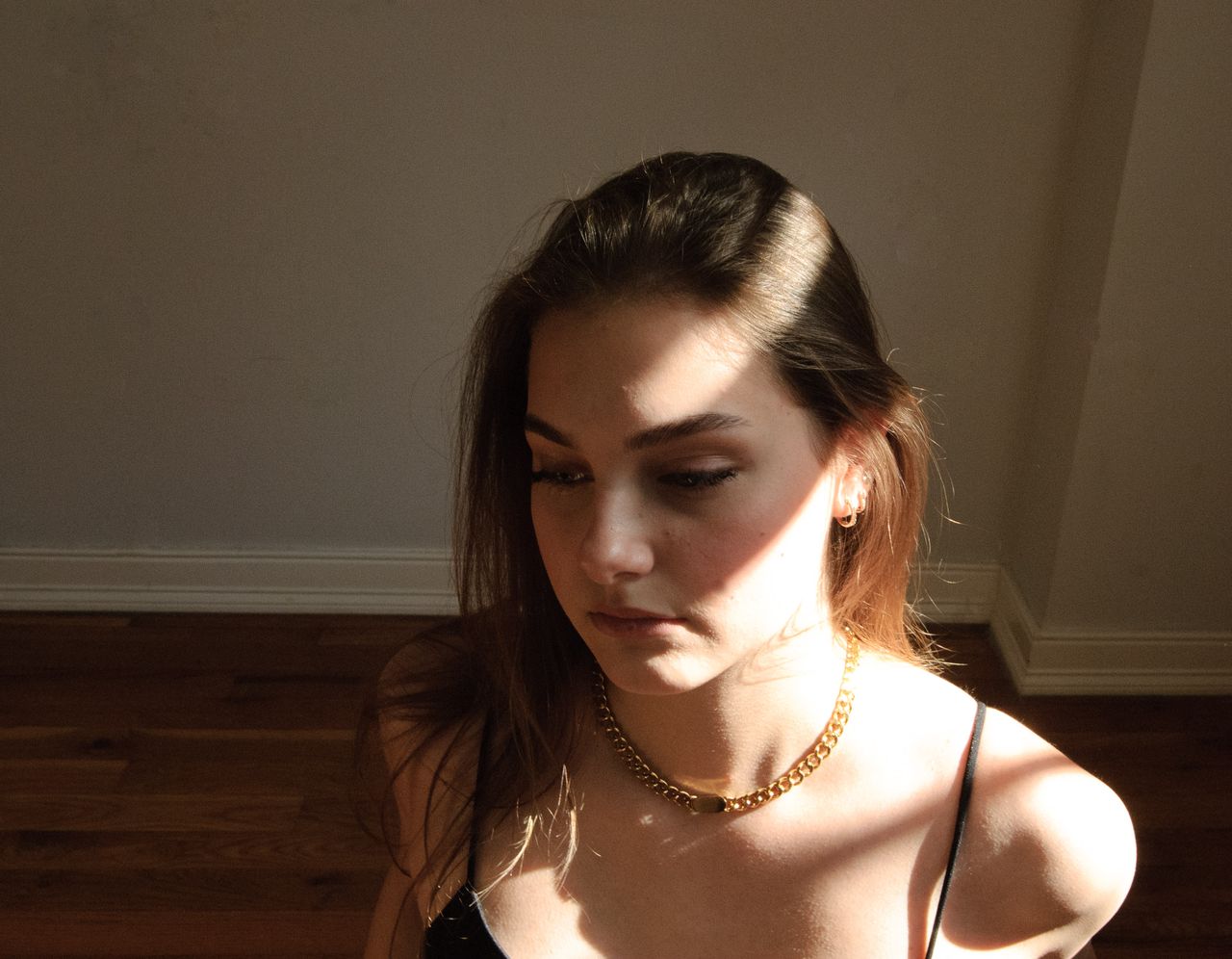 Mia Fantalin indoors in hard afternoon sunlight, wearing a black top and a gold chain necklace